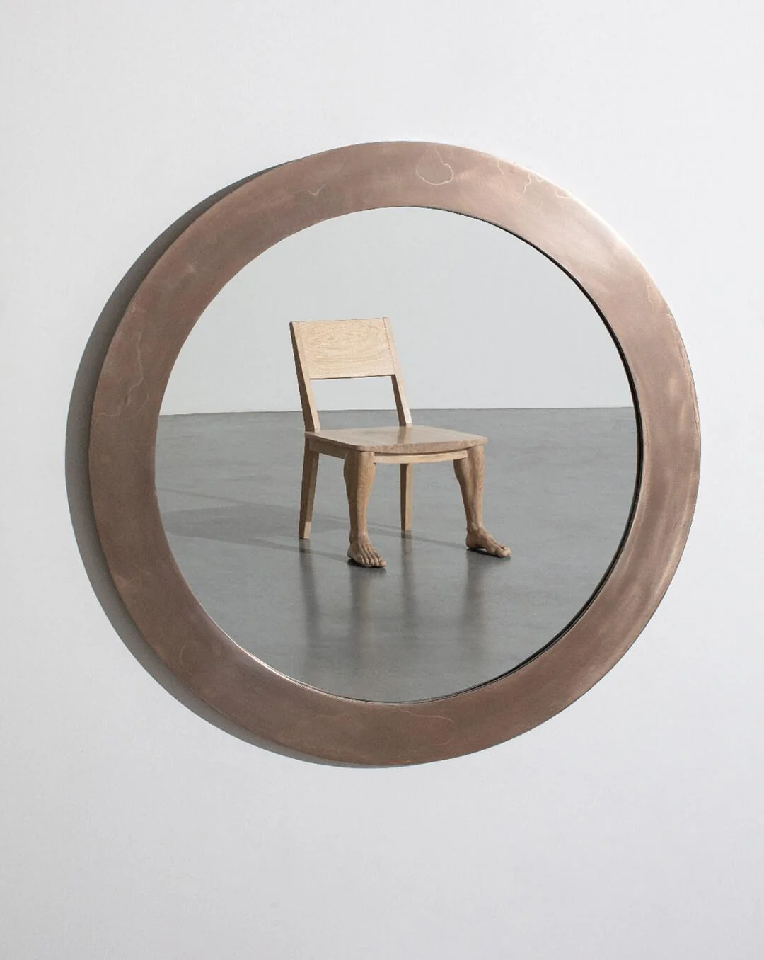 Espejo circular que refleja una silla de madera con patas humanas